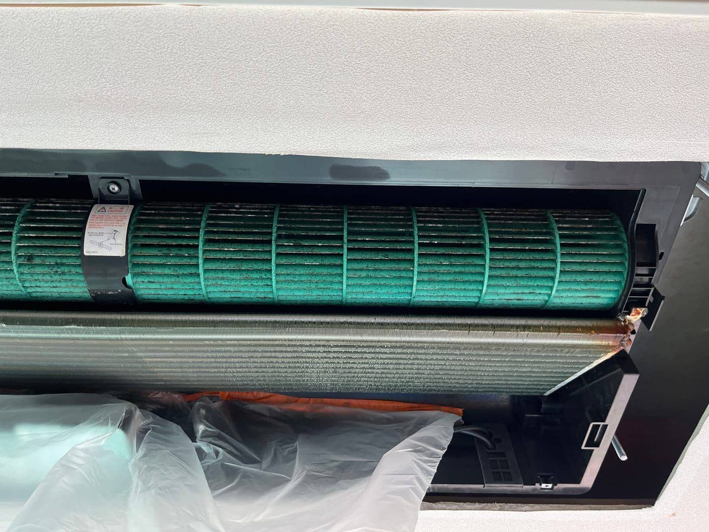 천장형 에어컨 내부 녹색 횡류팬 날개에 검은 점 오염이 퍼져 있고 아래로 열교환 코일이 보이는 모습.